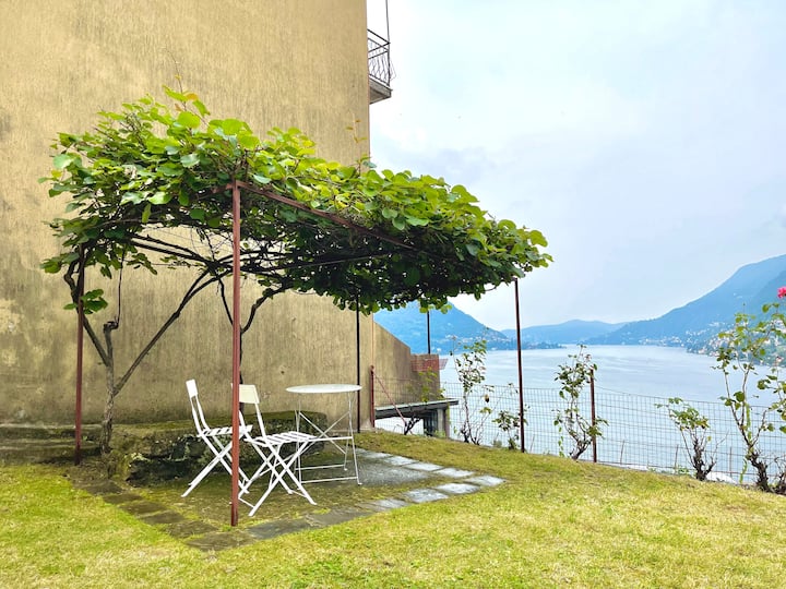 White bistro table under the kiwi-covered pergola with the lake beyond